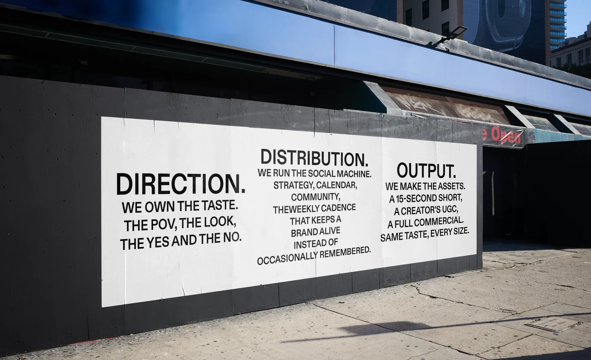 A Yes wall mural on a city street, three columns. Direction: we own the taste, the POV, the look, the yes and the no. Distribution: we run the social machine, strategy, calendar, community, the weekly cadence that keeps a brand alive instead of occasionally remembered. Output: we make the assets, a 15-second short, a creator's UGC, a full commercial, same taste every size.